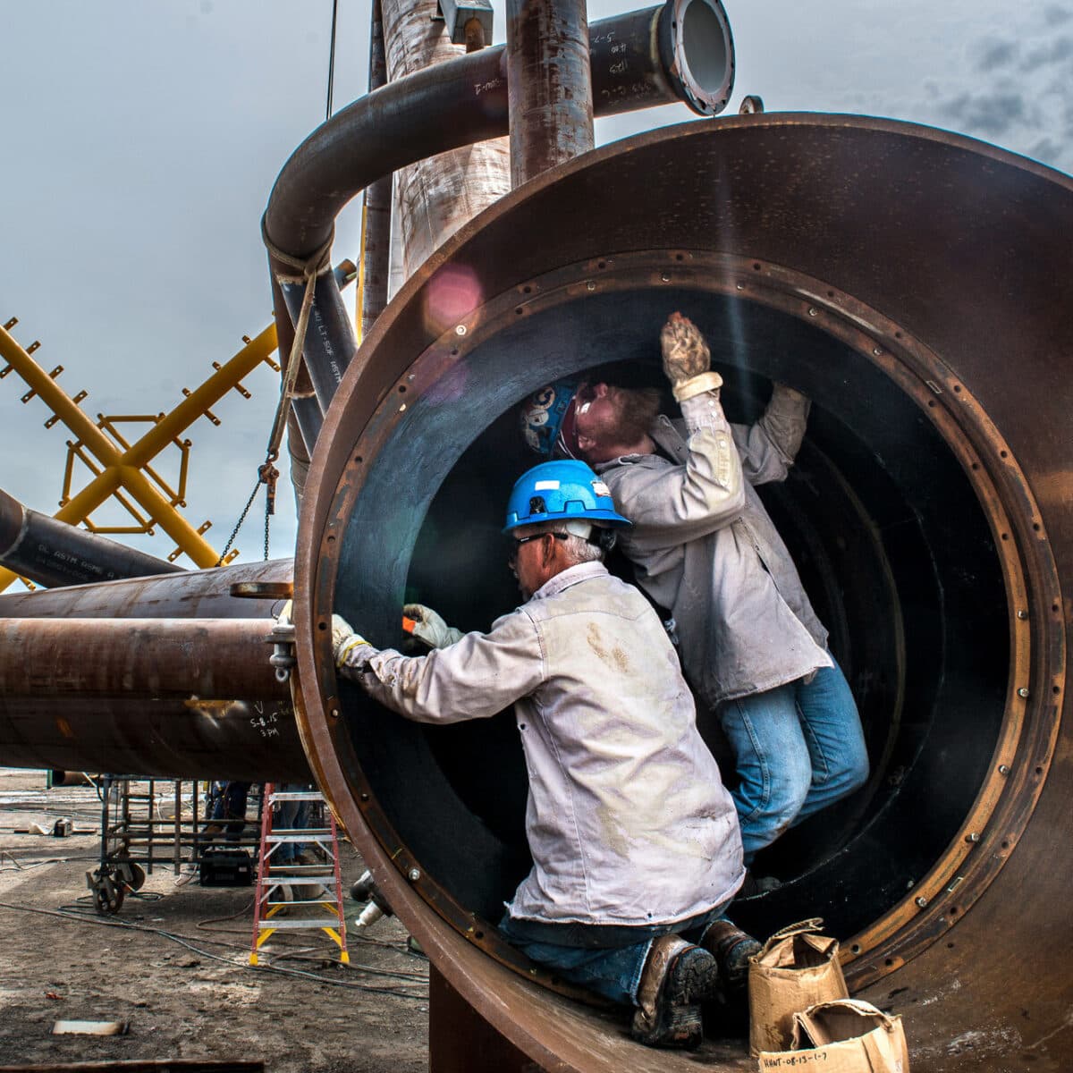 Two men in hard hats working inside a metal pipe