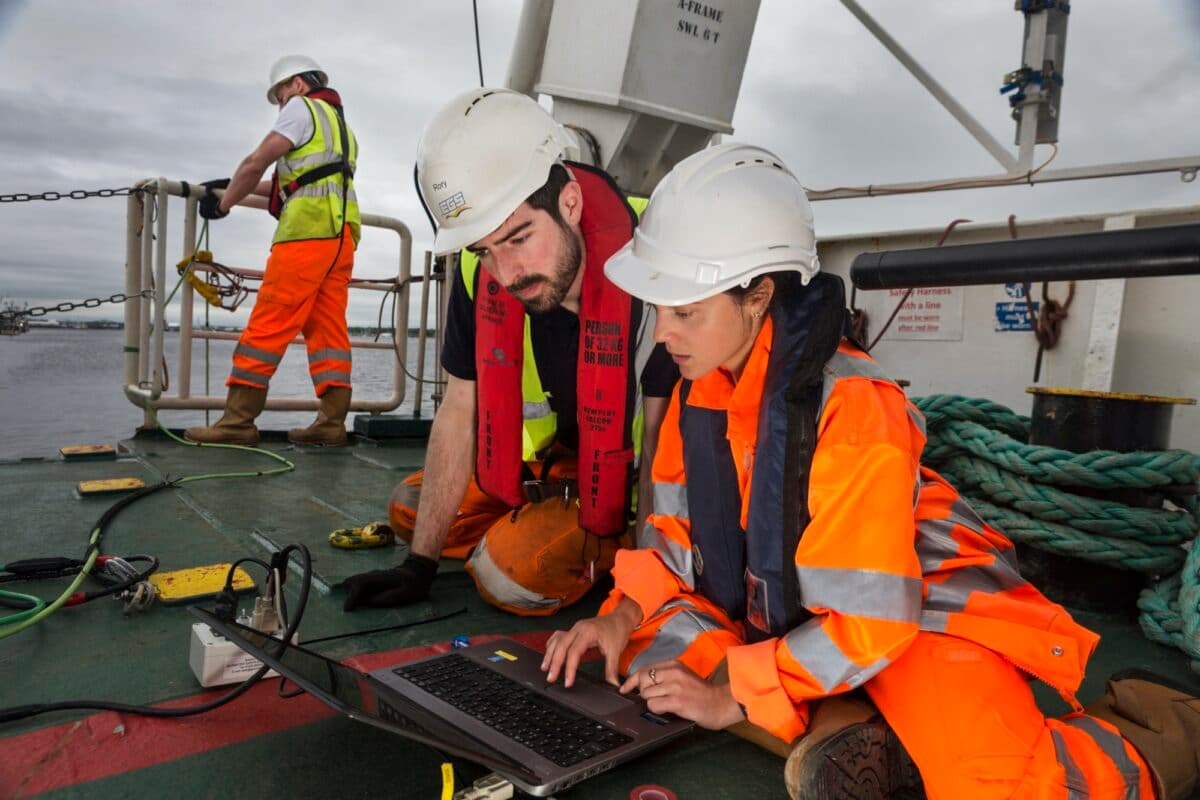 A man and woman wearing hard hats work on a wind turbine