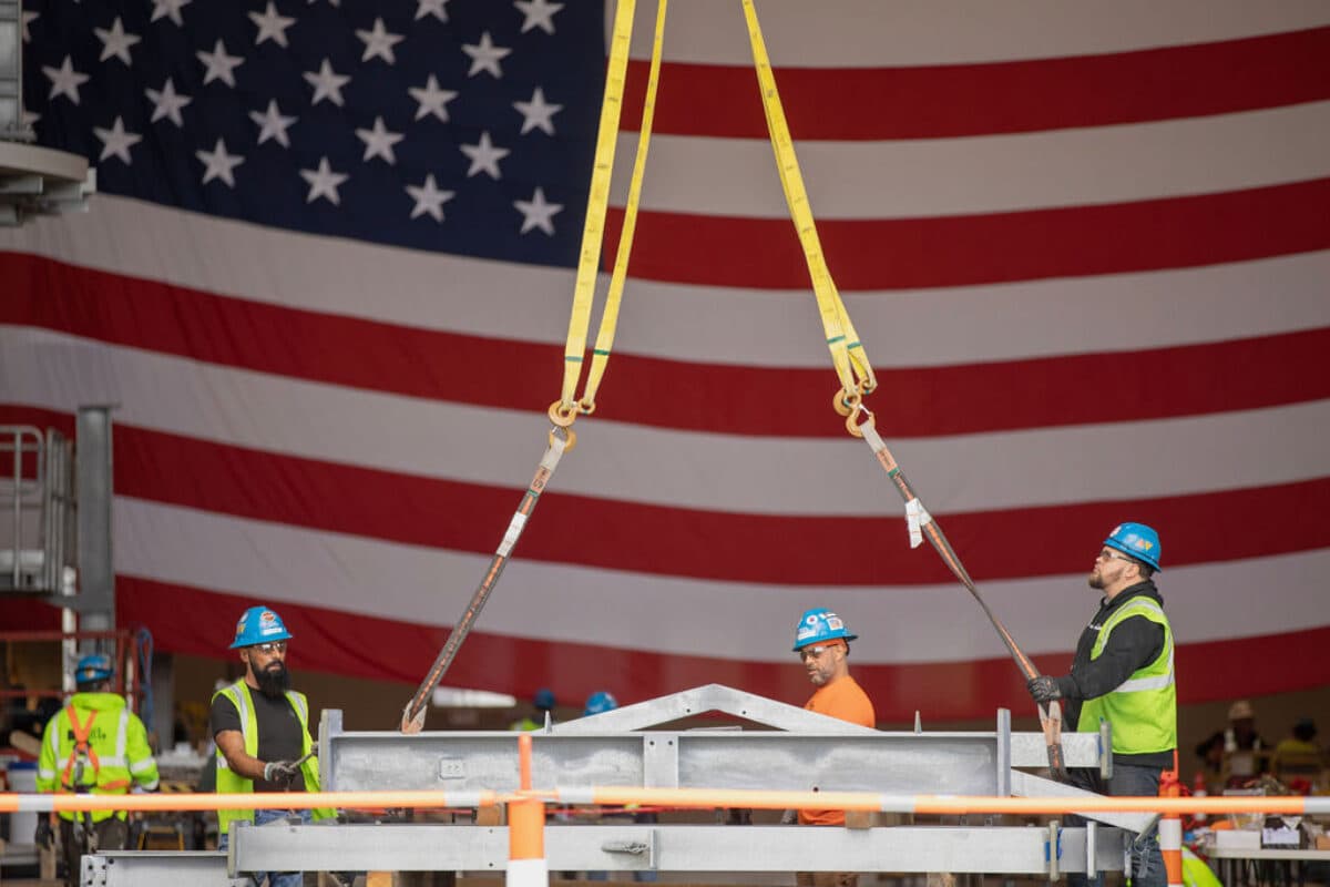 Tradesmen work in front of a large American flag